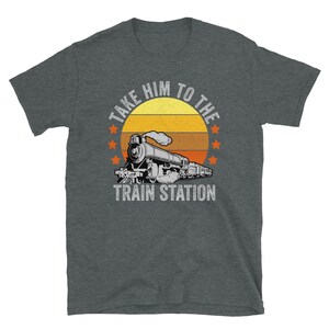 May include: A dark heather grey t-shirt with a vintage-style graphic of a train with the text "Take Him To The Train Station".