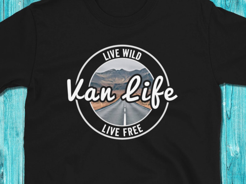 May include: Black t-shirt with a white circle graphic that says "Live Wild Van Life Live Free" with a picture of a road through a mountain landscape.