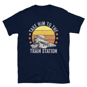 May include: Navy blue t-shirt with a vintage-style illustration of a train engine and the text "Take Him To The Train Station".