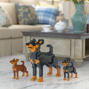 Pode incluir: Três cães de brinquedo em miniatura de plástico preto e castanho, feitos com blocos de construção. Os cães estão em pé sobre uma superfície branca em frente a uma mesa de café de madeira.