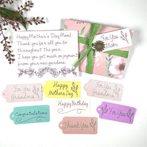 May include: A gift wrapped in pink floral paper with a green ribbon and a sunflower accent. Includes gift tags with phrases like "For You Mom," "Happy Mother's Day," and "Congratulations." A handwritten card reads "Happy Mother's Day Mom!"