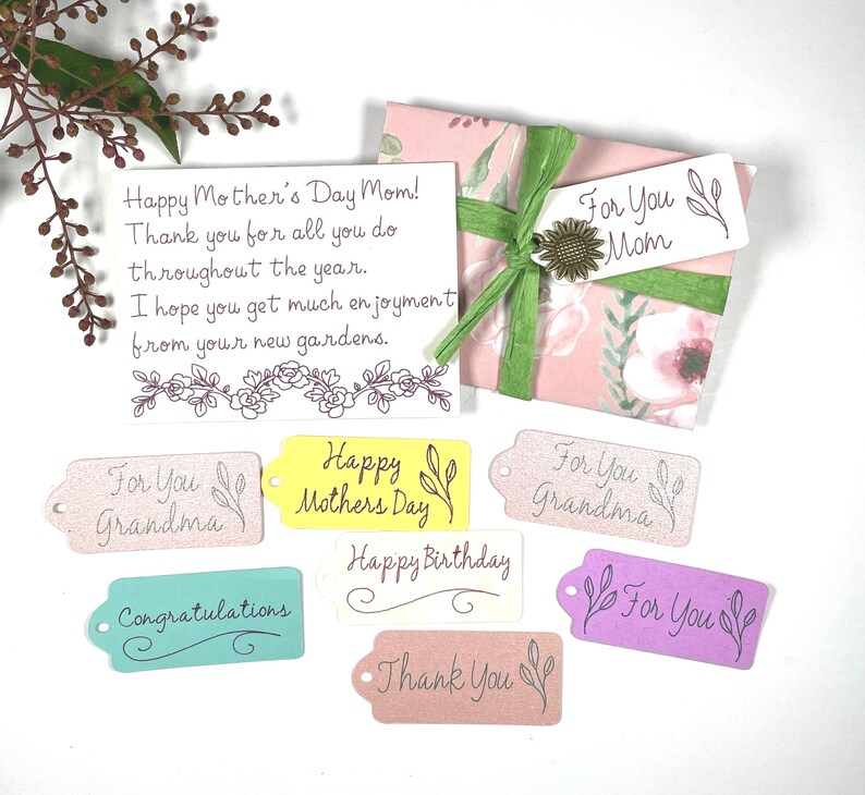 May include: A gift wrapped in pink floral paper with a green ribbon and a sunflower accent. Includes gift tags with phrases like "For You Mom," "Happy Mother's Day," and "Congratulations." A handwritten card reads "Happy Mother's Day Mom!"