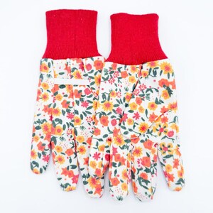 May include: A pair of gardening gloves with a white background. The gloves have a red cuff and a floral pattern of orange, yellow, and red flowers on a white background. The gloves are designed for gardening.