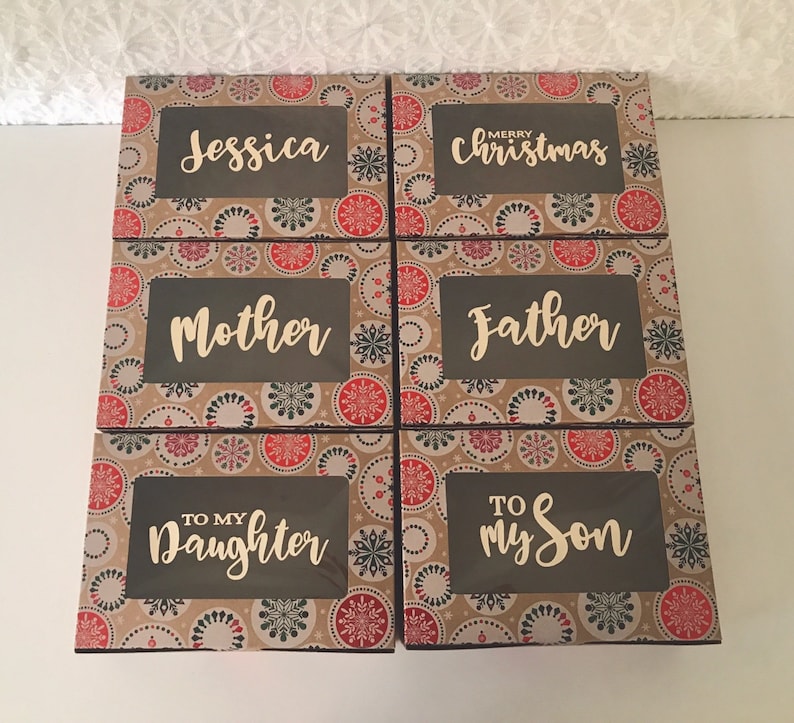 K&ouml;nnte beinhalten: Sechs kleine Geschenkboxen mit einem braunen und wei&szlig;en Schneeflockenmuster. Die Boxen haben ein transparentes Fenster auf der Vorderseite und jede Box tr&auml;gt eine andere Inschrift. Die Inschriften sind: "Jessica", "Frohe Weihnachten", "Mutter", "Vater", "An Meine Tochter", und "An Meinen Sohn".