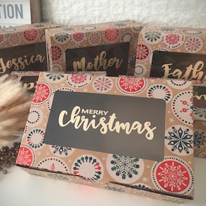 May include: Four brown gift boxes with a snowflake pattern and clear windows. The boxes are labeled "Jessica", "Mother", "Father", and "Merry Christmas".