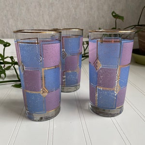 May include: Three clear glass tumblers with a geometric pattern of blue and purple squares with gold trim.