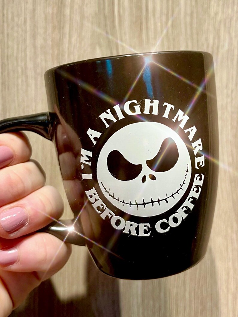 Puede incluir: Taza de cer&aacute;mica negra con el texto "I'm a Nightmare Before Coffee" en un dise&ntilde;o circular. El dise&ntilde;o presenta una cara blanca de Jack Skellington. La taza tiene un asa negra.