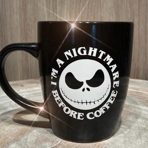 Puede incluir: Taza de cer&aacute;mica negra con un gr&aacute;fico blanco de la cara de un personaje de "Pesadilla antes de Navidad". El texto alrededor de la cara dice "I'M A NIGHTMARE BEFORE COFFEE."