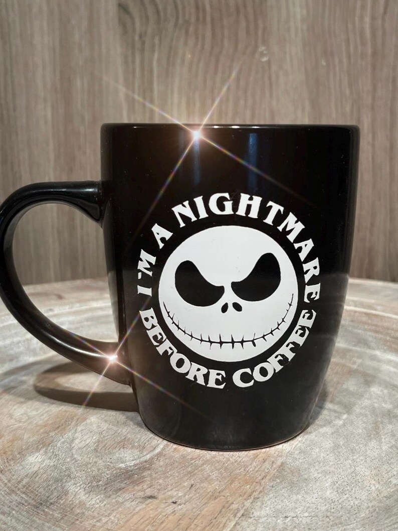 Puede incluir: Taza de cer&aacute;mica negra con un gr&aacute;fico blanco de la cara de un personaje de "Pesadilla antes de Navidad". El texto alrededor de la cara dice "I'M A NIGHTMARE BEFORE COFFEE."
