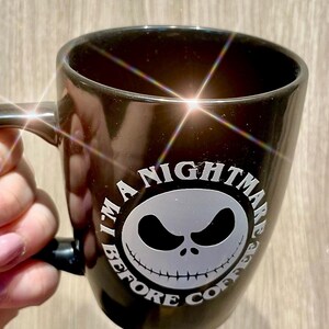 Puede incluir: Taza de cer&aacute;mica negra con un gr&aacute;fico blanco de la cara de Jack Skellington de "Pesadilla antes de Navidad". El texto "I'M A NIGHTMARE BEFORE COFFEE" est&aacute; impreso alrededor de la cara. La taza tiene un asa.