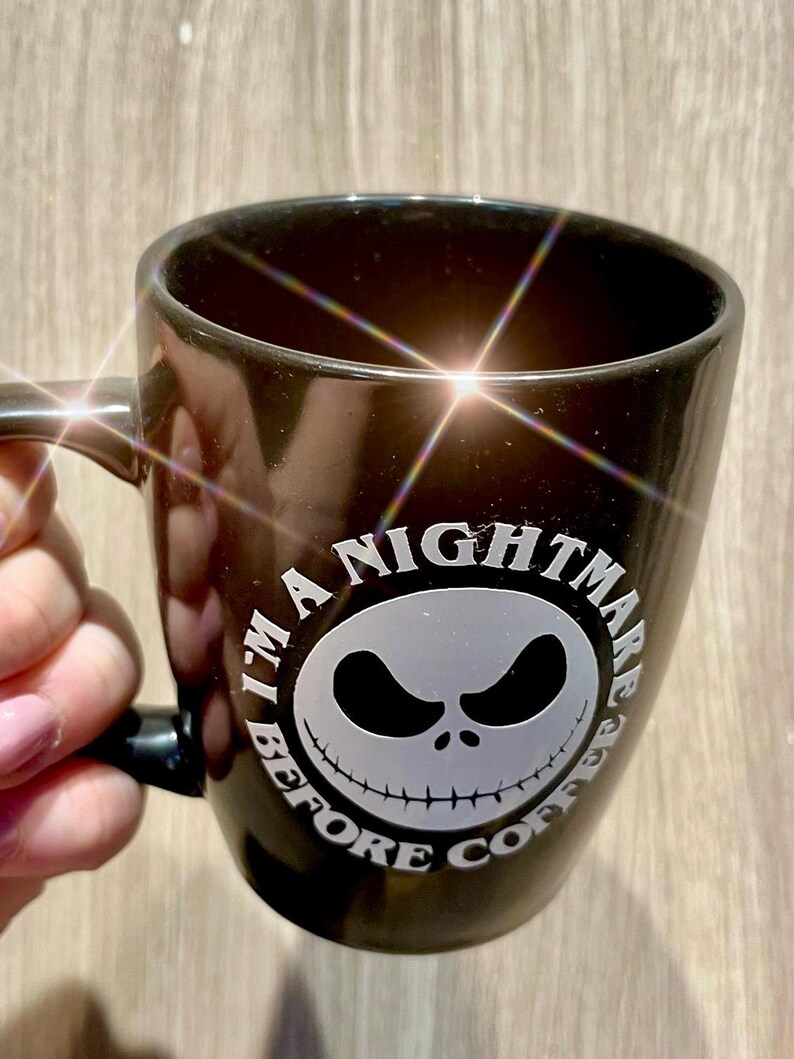 Puede incluir: Taza de cer&aacute;mica negra con un gr&aacute;fico blanco de la cara de Jack Skellington de "Pesadilla antes de Navidad". El texto "I'M A NIGHTMARE BEFORE COFFEE" est&aacute; impreso alrededor de la cara. La taza tiene un asa.