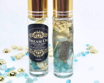 Puede incluir: Dos botellas de vidrio transparente con tapas doradas llenas de cristales azules y verdes y escamas doradas. Las botellas están etiquetadas con "DREAM OIL" y "DREAM".