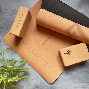 May include: A set of cork yoga blocks and a cork yoga mat with the text "Auswell." printed on them. The mat is rolled up and the blocks are stacked on top of the mat.