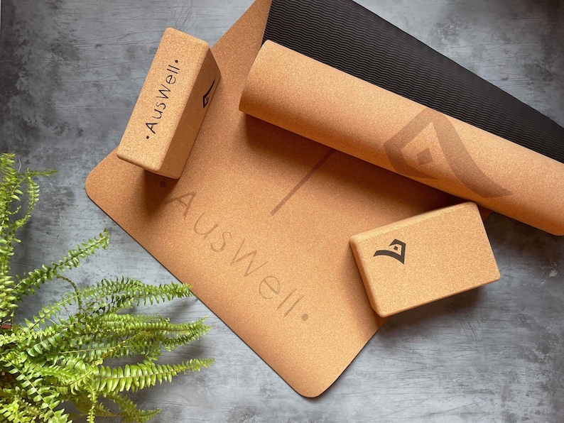 May include: A set of cork yoga blocks and a cork yoga mat with the text "Auswell." printed on them. The mat is rolled up and the blocks are stacked on top of the mat.
