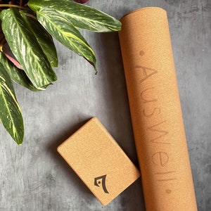May include: A brown cork yoga mat with the word "Auswell" printed on it. A brown cork yoga block with the Auswell logo is also pictured.