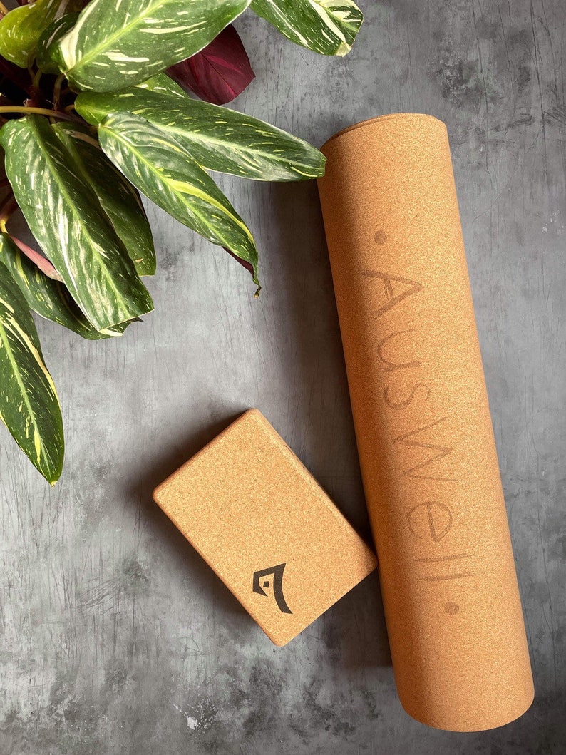 May include: A brown cork yoga mat with the word "Auswell" printed on it. A brown cork yoga block with the Auswell logo is also pictured.