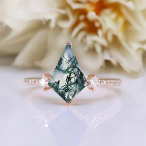 Puede incluir: Un anillo de oro rosa con una piedra preciosa de ágata verde musgo en forma de cometa. El anillo tiene dos diamantes más pequeños a cada lado de la piedra principal.
