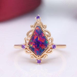 May include: A gold-colored ring featuring a large, multi-colored opal stone in a kite shape. The opal displays shades of red, blue, and purple. The ring is adorned with small purple gemstones and an ornate, filigree design.