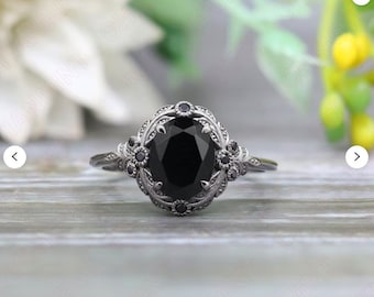 May include: A silver ring with a large black oval gemstone surrounded by smaller black gemstones and intricate silver detailing.