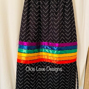 May include: Black skirt with a white chevron pattern. The skirt features a horizontal band of rainbow-colored ribbons. The text "Okie Love Designs" is printed on the skirt.