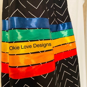 May include: Black fabric with a white chevron pattern. The design features bands of colorful satin ribbon in blue, green, yellow, orange, and red. The text "Okie Love Designs" is visible on the yellow ribbon.