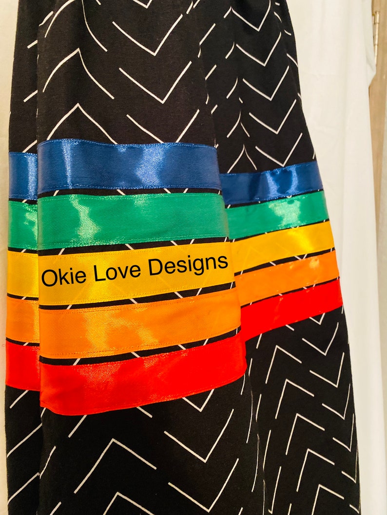 May include: Black fabric with a white chevron pattern. The design features bands of colorful satin ribbon in blue, green, yellow, orange, and red. The text "Okie Love Designs" is visible on the yellow ribbon.