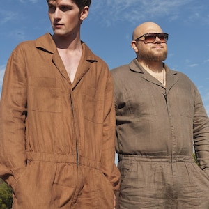 May include: Two people wearing brown and beige linen jumpsuits. The person on the left is wearing a brown jumpsuit and the person on the right is wearing a beige jumpsuit. Both people are standing in a field.