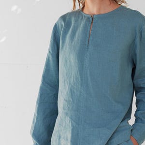 May include: A long-sleeved shirt in a light blue color with a round neckline and a small slit at the neckline.