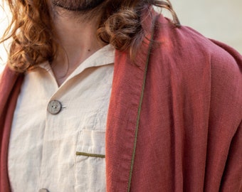 May include: A rust-colored linen robe with a green trim. The robe is worn over a white linen shirt with buttons.