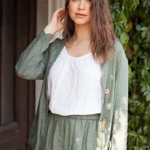 May include: A woman wearing a green linen jacket and matching pants. The jacket has a button closure and the pants have an elastic waistband.