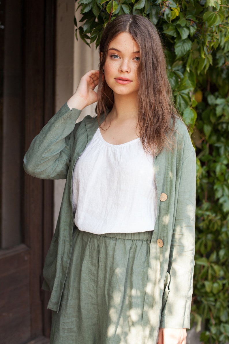 May include: A woman wearing a green linen jacket and matching pants. The jacket has a button closure and the pants have an elastic waistband.
