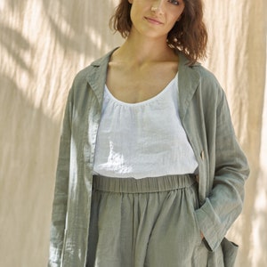 May include: A woman wearing a green linen jacket and matching pants. The jacket has a collar and long sleeves. The pants have a drawstring waist and pockets.