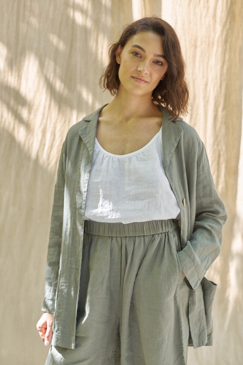 May include: A woman wearing a green linen jacket and matching pants. The jacket has a collar and long sleeves. The pants have a drawstring waist and pockets.