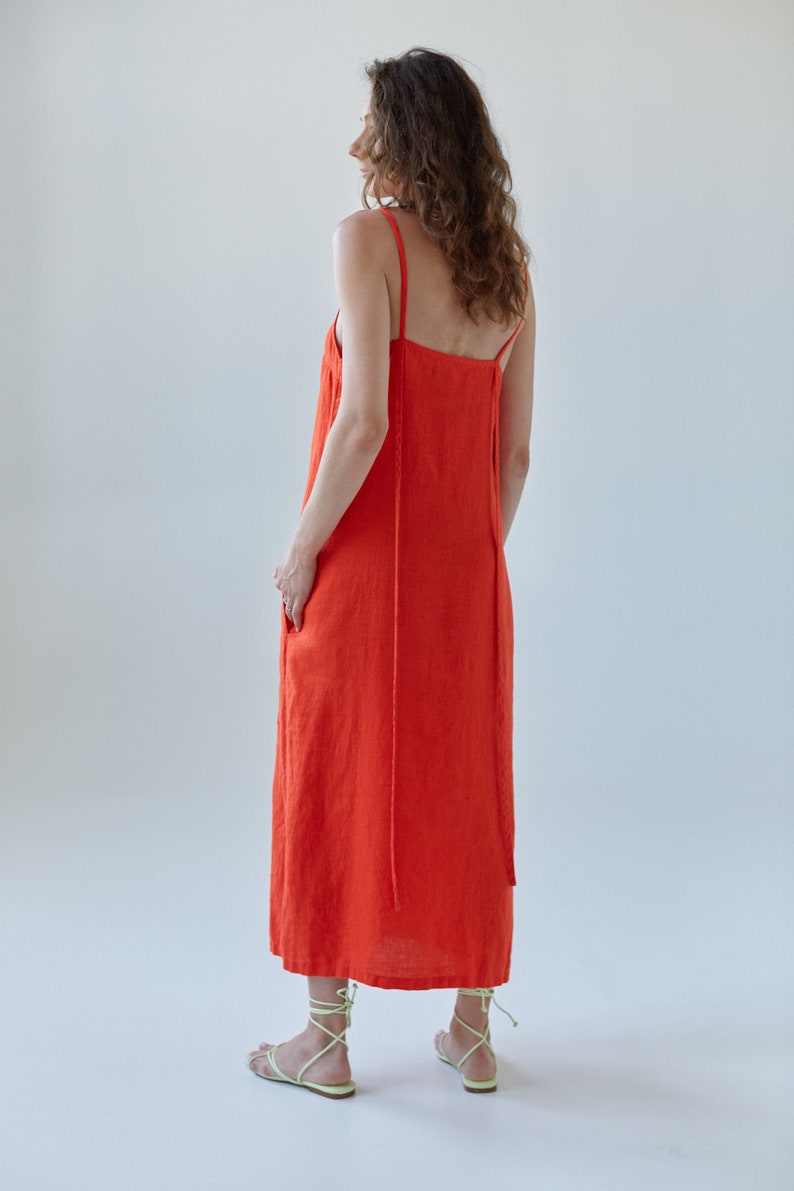 May include: A bright orange maxi dress with thin straps. The dress is made of a lightweight fabric and has a relaxed fit.
