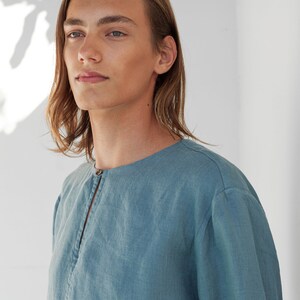 May include: A light blue linen shirt with a long sleeve and a button closure at the neck.
