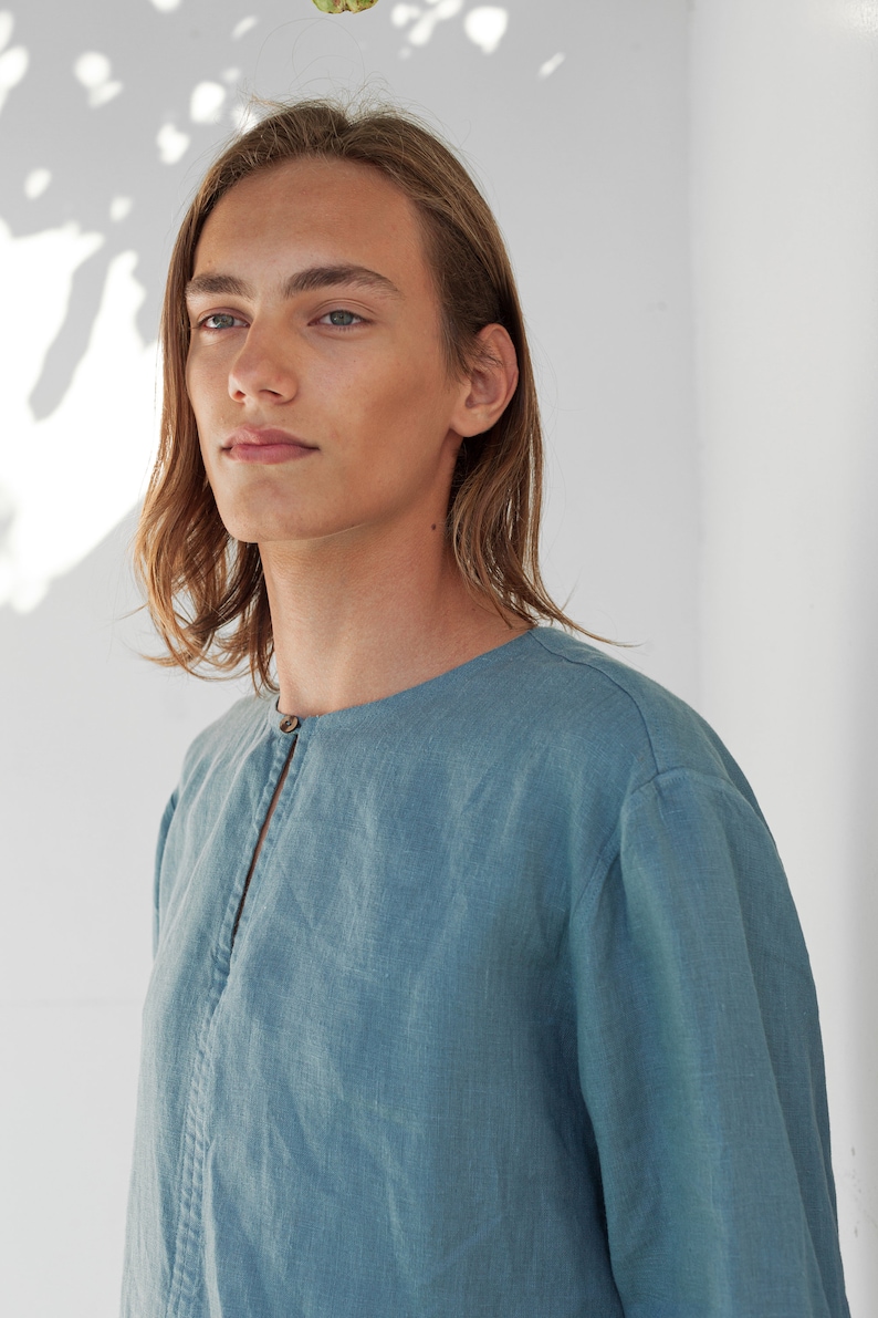May include: A light blue linen shirt with a long sleeve and a button closure at the neck.
