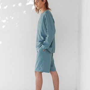 May include: A person wearing a light blue linen shirt and matching shorts. The person is standing on a white wooden floor.