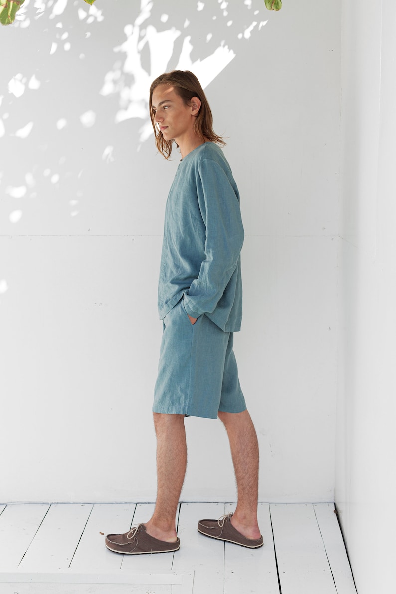 May include: A person wearing a light blue linen shirt and matching shorts. The person is standing on a white wooden floor.