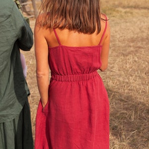 May include: A woman wearing a red linen dress with thin straps and a gathered waist.