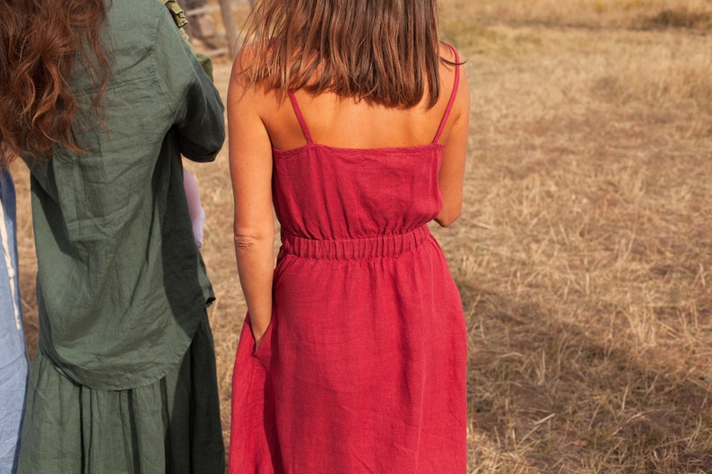 May include: A woman wearing a red linen dress with thin straps and a gathered waist.
