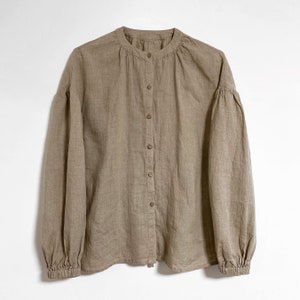 Op de afbeelding: Een bruin linnen shirt met een staande kraag en knoopsluiting. Het shirt heeft lange mouwen met elastische manchetten en een ontspannen pasvorm.