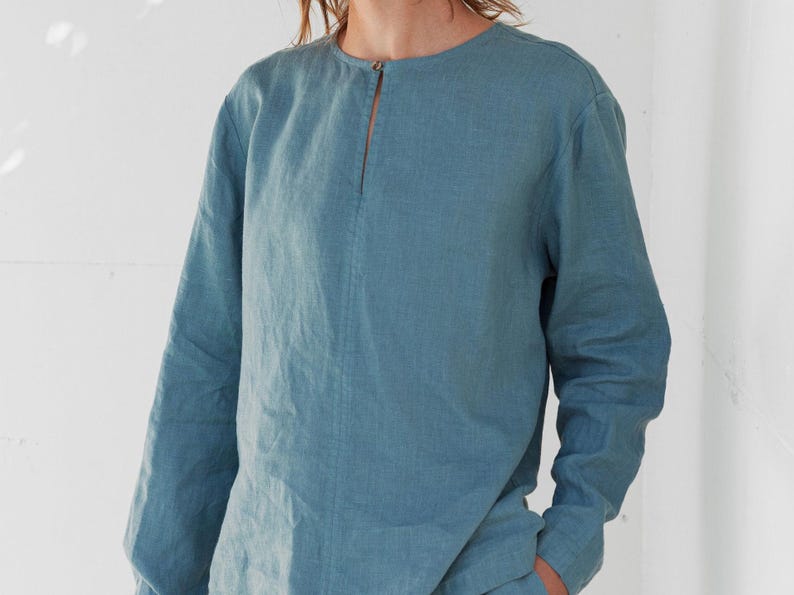 May include: A long-sleeved shirt in a light blue color with a round neckline and a small slit at the neckline.
