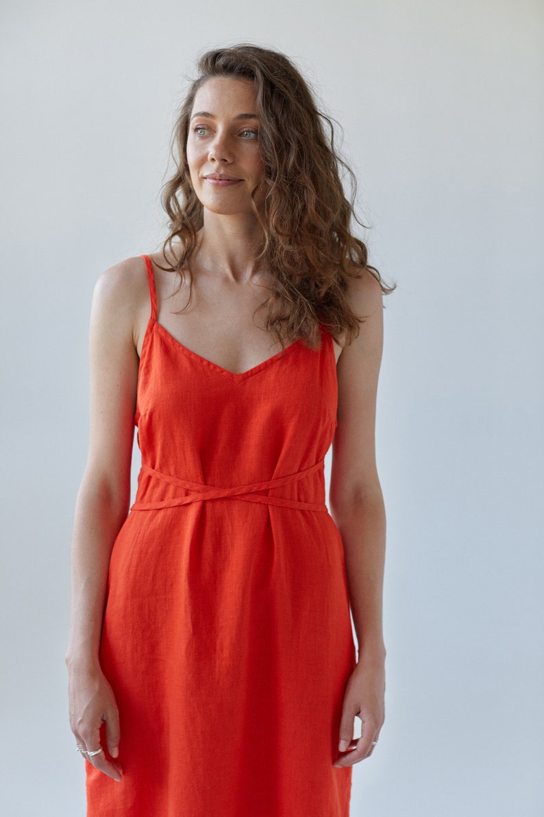 May include: A woman wearing a bright orange linen dress with a criss-cross detail at the waist.