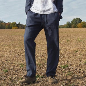 May include: A pair of dark blue linen pants with a drawstring waist. The pants are worn by a person standing in a field.