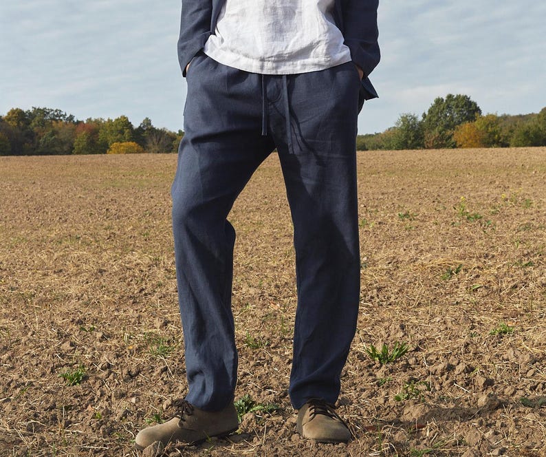 May include: A pair of dark blue linen pants with a drawstring waist. The pants are worn by a person standing in a field.