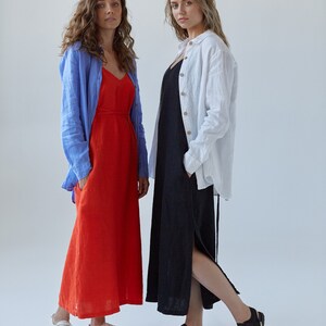May include: Two women wearing long dresses. The woman on the left is wearing a red dress with a blue shirt over it. The woman on the right is wearing a black dress with a white shirt over it. Both women are wearing sandals.