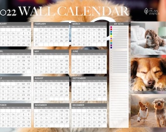 Op de afbeelding: Een wandkalender voor 2022 met schattige honden in verschillende poses. Elke maand wordt weergegeven met een rooster van nummers, en de kalender bevat een sectie voor notities en een "Mijn sleutels"-checklist.