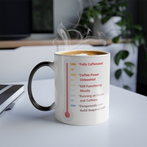 May include: White ceramic coffee mug with a black handle. The mug has a thermometer design with a red liquid level and text that reads "Fully Caffeinated", "Coffee Power Unleashed", "Still Functioning Mostly", "Running on Fumes... and Caffeine", and "Dangerously Low - Refill Required ASAP".