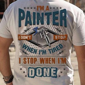 May include: Light gray t-shirt with the text "I'M A PAINTER" in blue and orange. The shirt features a graphic of a paint sprayer and the phrases "I DON'T STOP WHEN I'M TIRED, I STOP WHEN I'M DONE."