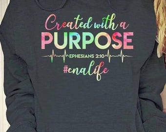 May include: A dark gray hoodie with a rainbow-colored graphic that says "Created with a PURPOSE" with a heartbeat graphic and the text "EPHESIANS 2:10" below it. The hashtag "#cnalife" is printed below the heartbeat graphic.